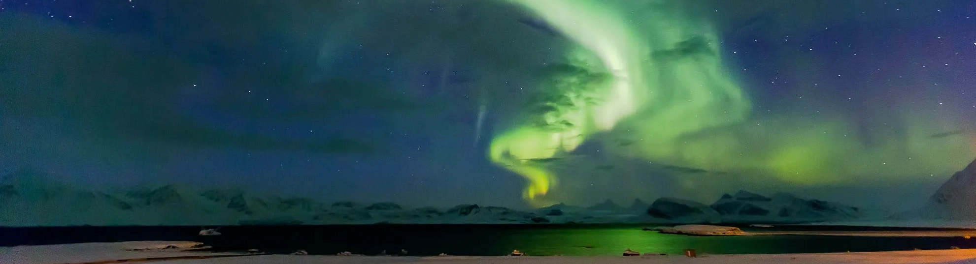 A ribbon of green aurora over mountains and water