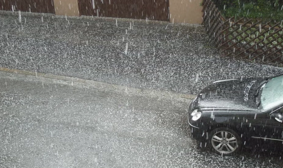 Small hail falling onto a street with a car visible in the lower right.