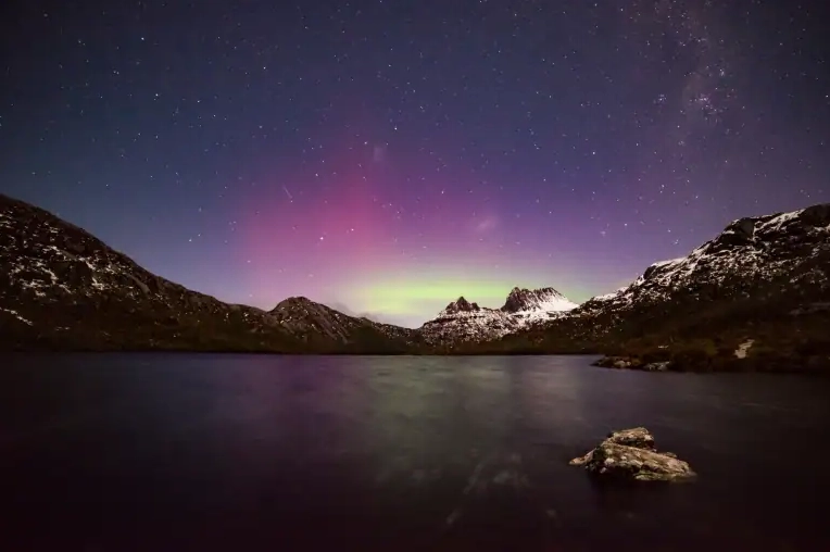The Aurora Australis shining in purple and green hues behind snow-capped peaks